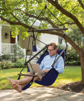 Man relaxing outdoors in a Deluxe Hanging Hammock Sky Chair For Chill Sessions With Pillow And Drink Holder Solid Wood Spreader Bar Weather Resistant For Indoor Or Outdoor Porch Patio Yard Tree Navy Blue Supports Up To 250 Lbs.
