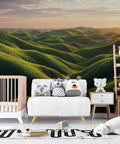 Custom Peel And Stick Wall Mural Featuring Lush Green Meadow Scene in a child’s room with soft toys and crib.