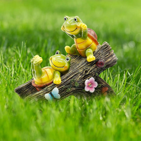 Two playful turtle figurines on a log with flowers and a butterfly in a grassy garden setting.