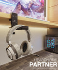 Under Desk Headphone Stand With Foldable Arm Space Saving Aluminum Headset Hanger For Gaming Headphones Desk Clamp Fits Desks Up To 50mm Thick Or Slim 5mm Mounts Flat Against Wall When Not In Use Universal Fit Black holding a headset.