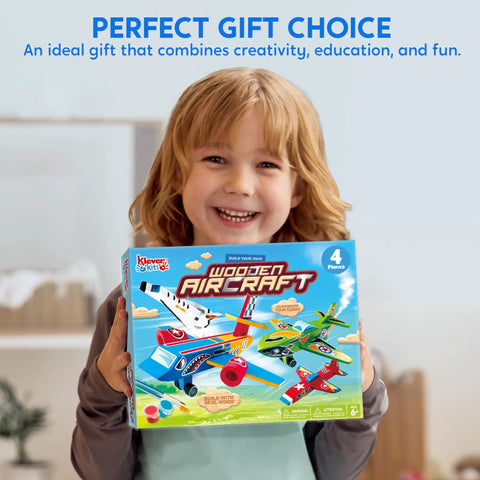Child holding All In One DIY Wooden Airplane Craft Kit For Kids Ages 6 To 12 Totally Kid Friendly Build Four Aircraft And Paint With Six Paint Tubs Two Brushes And Stickers Easy To Follow Instructions Great Birthday Gift For Young Builders box