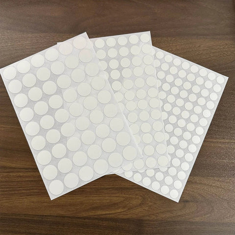 Sheets of White Screw Hole Cover Set Including 290 Pieces In Three Sizes 12mm 15mm And 21mm Self Adhesive PVC Caps on wood surface