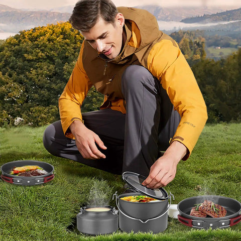 Man using 22 Piece Camping Cookware Mess Kit For Four With Hanging Pot Pan Kettle Base Dishes Cups Spoons Forks And Carry Bags Outdoor Cooking Set For Camping Hiking And Picnics in a scenic outdoor setting.
