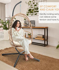 Woman relaxing in hanging egg chair with stand and footrest for indoor outdoor use, chill wicker swing chair with aluminum steel frame.