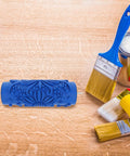 Pro-Level Rubber Texture Paint Roller For Walls And Ceilings DIY Decor Game Changer sitting on a wooden surface with brushes.