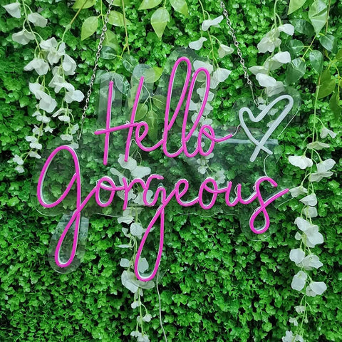 Hello Gorgeous Pink LED Neon Sign For Wall Decor, 21 Inch Neon Light hanging on greenery with vines, acrylic back visible.