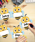 Bee Cutouts For Classroom Decorations 50 Pack Name Tags And Desk Nameplates Cute Bee Style Labels on a wooden desk surface.