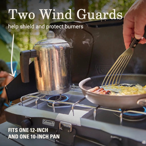 Triton Two Burner Propane Camp Stove With Wind Guards showing burners in action with cooking pot and spatula.