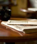 Sleek White Second Gen Ereader Features A Sharp Six Inch Screen And Free 3G Wireless To Pull Down Books Anywhere on a wooden table next to a coffee cup.