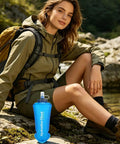 Woman hiking by river with Foldable Hydration Bottle For Hiking And Running, 11.42 Inch Squeeze Bladder With Leakproof Caps nearby.