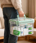 Grab And Go See Through Medicine Storage Box Set With Lids 2 Pack Portable First Aid Organizer With Handle Stackable Medical Supply Storage For Family Home Office Bathroom Bedroom Green clear box held by hand