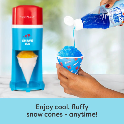 Next Level Electric Shaved Ice And Snow Cone Maker pouring blue syrup over a fluffy snow cone in a cup on a countertop.