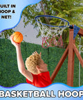 Child playing basketball on Applewood Cedar Wooden Swing Set With Double A Frame And Easy Setup, 32 Inch Two Person Saucer And Sling Swings, 6 Foot Wavy Slide, Covered Fort With Rock Wall, Chalkboard, Sandbox And Basketball Hoop For Backyard Fun