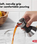 Hand pouring liquid using Stainless Steel Two Sided Jigger With Flip Measurements, Soft Non Slip Grip For Easy Pouring, into a glass.
