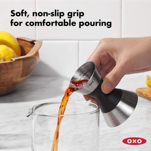 Hand pouring liquid using Stainless Steel Two Sided Jigger With Flip Measurements, Soft Non Slip Grip For Easy Pouring, into a glass.