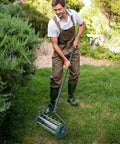 Man using 17 Inch Heavy Duty Rolling Lawn Aerator with sharp spikes and anti-slip handle on garden lawn for manual aeration tool.