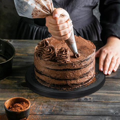 Close-up of a hand piping chocolate frosting on a layered cake using a piping bag, showcasing cake decorating techniques.
