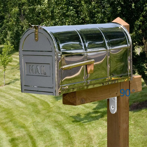 Stainless steel mailbox mounted on wooden post in a grassy yard with trees in the background.