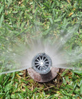 Heavy Duty 4 Inch Pop Up Lawn Sprinkler Head Serving A Solid 15 Foot Adjustable Spread with water spray over green grass.
