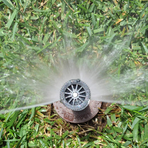 Heavy Duty 4 Inch Pop Up Lawn Sprinkler Head Serving A Solid 15 Foot Adjustable Spread with water spray over green grass.