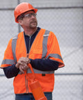 Man wearing High Visibility Sleeved Mesh Safety Vest With Brilliant Reflective Tape And Utility Pockets Class 3 at job site.
