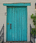 Turquoise wooden door with iron barn door pull handle, surrounded by cacti and lanterns.