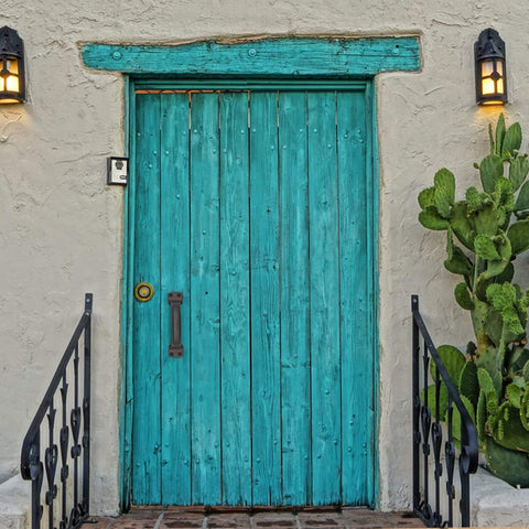 Turquoise wooden door with iron barn door pull handle, surrounded by cacti and lanterns.