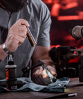 Person holding ProTac 1L-1AA 350-Lumen Compact Tactical LED Flashlight With Alkaline Battery Coyote Finish near a rifle on a table.