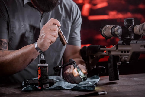 Person holding ProTac 1L-1AA 350-Lumen Compact Tactical LED Flashlight With Alkaline Battery Coyote Finish near a rifle on a table.