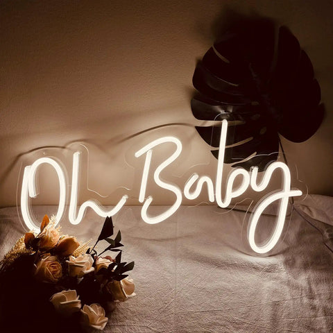 Oh Baby Neon Sign White LED Wall Decor with dimmable brightness and plug in power adapter, soft glow on a table setup with flowers.