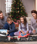 Family playing with Electric Train Set For Kids With Steam Locomotive And Cargo Cars Tracks And Railway Kit near Christmas tree