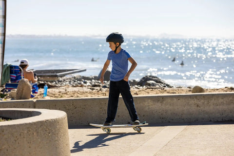 Child riding RipStik RipSurf Caster Board For Street Surfing With Traction Pad And Durable Poly Deck Two High Performance Wheels 10.5 Inch Deck CMYK Finish on pavement by the beach.