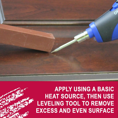 Quick Fill Burn In Stick Wood Filler In True Brown Shade being applied with a heat gun on hardwood surface for repairs.