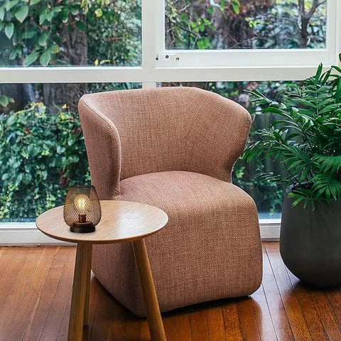 Set Of 4 Battery Operated LED Table Lanterns In Rustic Brown Metal Cage on a wooden table next to a fabric chair in a bright room.