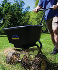 Person using Spyker P20 5010 50 Pound Capacity Broadcast Spreader for Fertilizer Grass Seed and Ice Melt in a green lawn