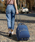 Person walking with Underseat 16-Inch Carry-On Luggage With Wheels, Softside Rolling Travel Bag, quilted blue polyester material