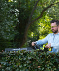 Pro Level 18V ONE PLUS Cordless Hedge Trimmer Featuring 55cm Double Edge Blades in use by a man trimming hedges.
