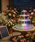 6.5W Solar Bird Bath Fountain With Lights on patio, 3 tier DIY water feature, detachable solar pump, surrounded by flowers at night