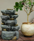 Solar Water Fountain Outdoor Garden 19.3 Inch Cascading Stone Design Five Tier Rock Feature Waterfalls beside potted plant