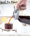 Pouring iced coffee from 32 Oz Mason Jar Cold Brew Pitcher With Strainer And Wide Mouth Glass Spout Lids For Fridge Iced Coffee Tea Lemonade Sun Tea 1 Quart Brew Maker Dishwasher Safe No Mess into a glass with lemon slice.