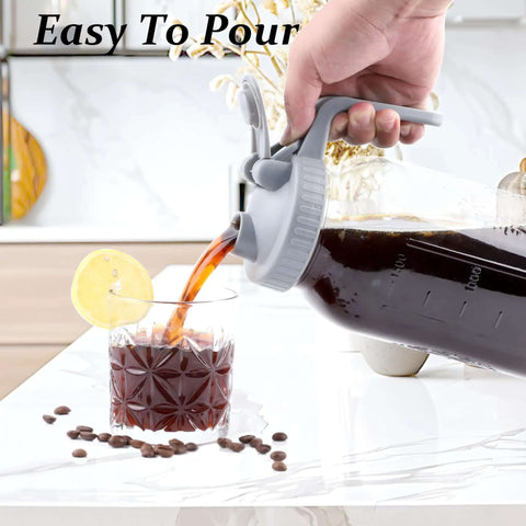 Pouring iced coffee from 32 Oz Mason Jar Cold Brew Pitcher With Strainer And Wide Mouth Glass Spout Lids For Fridge Iced Coffee Tea Lemonade Sun Tea 1 Quart Brew Maker Dishwasher Safe No Mess into a glass with lemon slice.