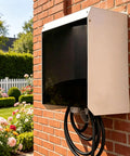 Beefy EV Charger Cover For Outdoor Wall Mount With Magnetic Flip Top and Tinted Window on a brick wall with garden backdrop.