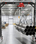 Heavy Duty Gantry Crane With 2200 Lb Capacity And Electric Hoist lifting metal pipes in a factory setting.