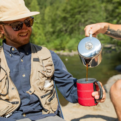 Pouring coffee from 3 Cup Percolator Coffee Pot In Glacier Stainless Steel With Silicone Handle into a red mug outdoors.