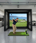 Man practicing golf swing in inflatable golf simulator enclosure with white projection screen in garage, portable practice net