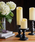 Realistic Moving Flame LED Candle Pillar With Scalloped Edge And Smooth Finish For A Cozy Glow Vanilla Honey Scented Ivory Timer Function Battery Operated 3 Inch By 4.5 Inch with black holder on wooden table