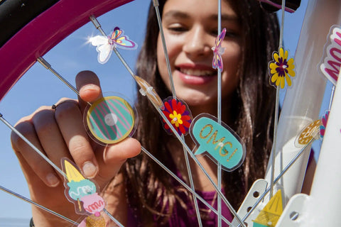 Kid smiling while attaching Totally Adorable Kids Bike Spoke Decorations Set With 36 Colorful Charms Featuring Dino, Flower And Butterfly Themes