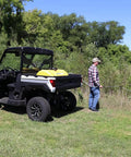 Man using 40 Gallon Yellow Sprayer Tank With Translucent Body Farm-Ready on utility vehicle for pesticide application in a field.