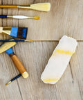 Heavy Duty Polyester Paint Roller Cover Refills on a wooden surface alongside various paint brushes, ideal for painting projects.