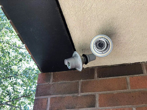 WiFi Floodlight Bulb Camera For Outdoor Security, 1080P Night Vision, mounted under a porch roof, brick wall visible
